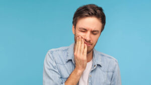 Man holding his jaw with tooth pain representing a dental emergency requiring prompt care