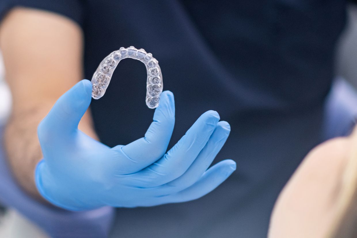 Dental professional holding a clear Invisalign aligner used to straighten teeth
